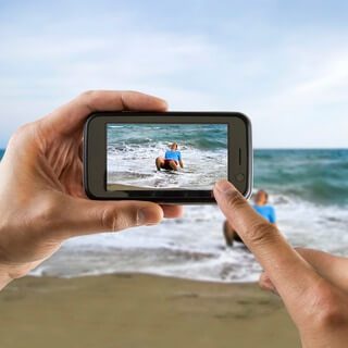 a person taking a picture of a beach with a cell phone.