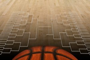 A basketball sits at the foreground on a wooden court with an empty March Madness bracket projection above it, suggesting the anticipation of exciting matchups and fierce competition.