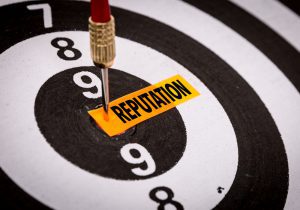 A dart pinned right on a label with the word "reputation" at the center of a dartboard, symbolizing the critical importance and precise aim required to hit and maintain a good reputation.