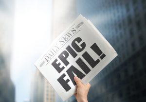 A person holds a newspaper that says "Epic Fail" on the front page.