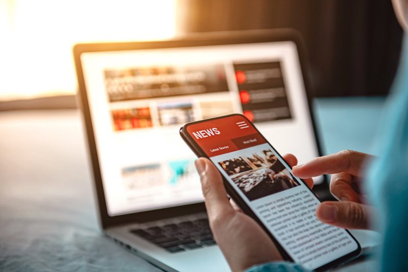 A person looks at an online newspaper using their laptop and smartphone.