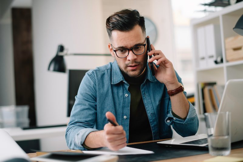 A man sits at a desk and is on the phone with a newspaper editor.