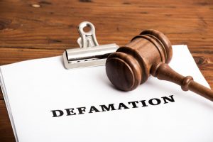 A gavel sits on a piece of paper with the word "defamation" on it.