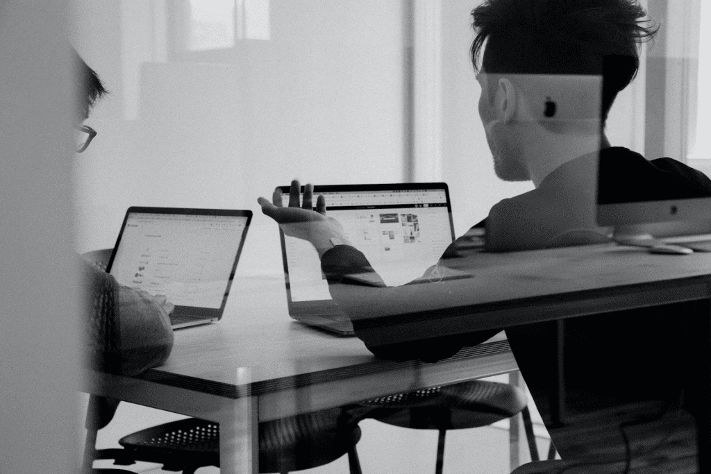 two people sitting at a table with laptops.