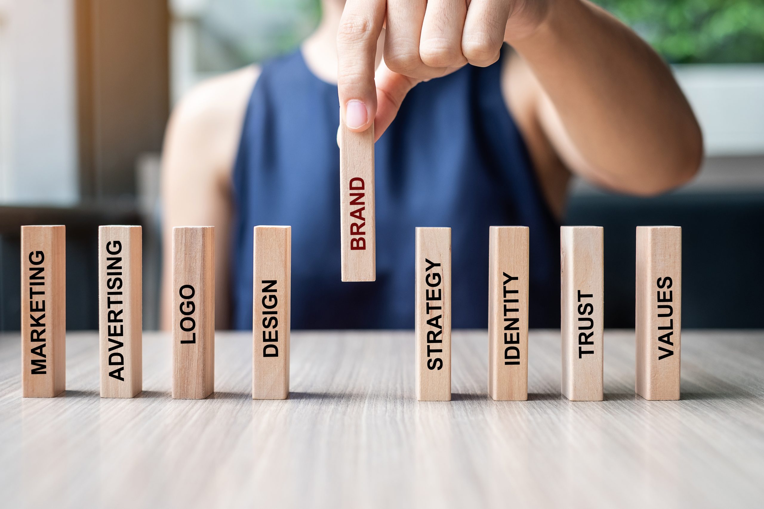 A woman is pointing to wooden blocks with the words brand and marketing.