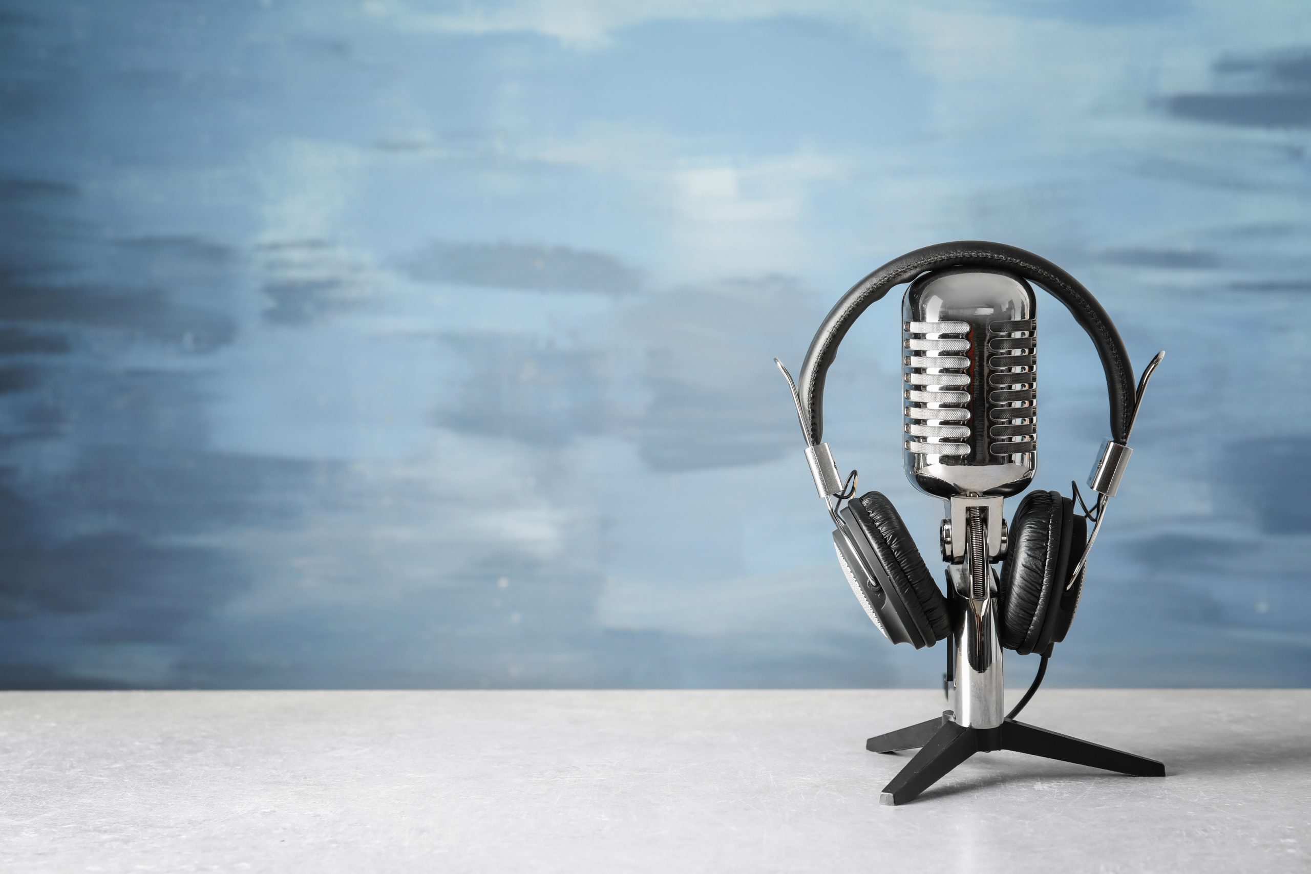 A microphone with headphones on a table against a blue background.