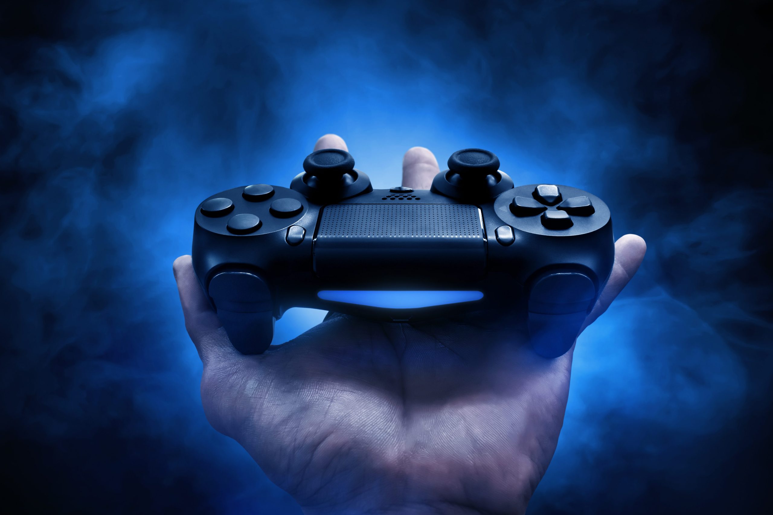 A hand holding a video game controller in front of a blue background.