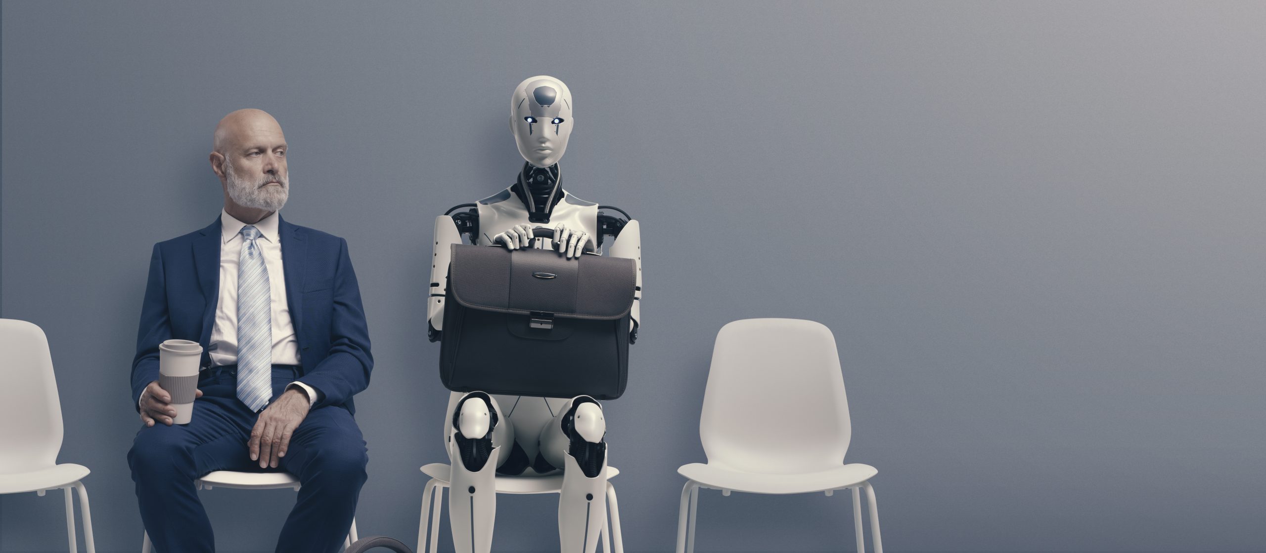 A man in a suit sits in a chair next to a robot.