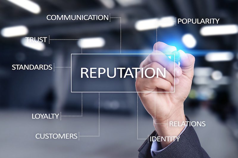 A person in a suit writes "REPUTATION" on a transparent board, linking related terms like communication, trust, standards, and loyalty—showcasing how the best reputation management services connect these elements for success.