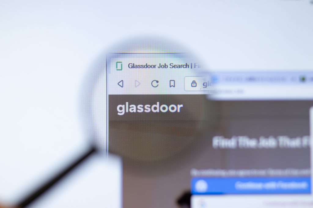 A magnifying glass is focusing on the Glassdoor website logo displayed on a computer screen. The browser address bar and part of the web page are visible in the background.