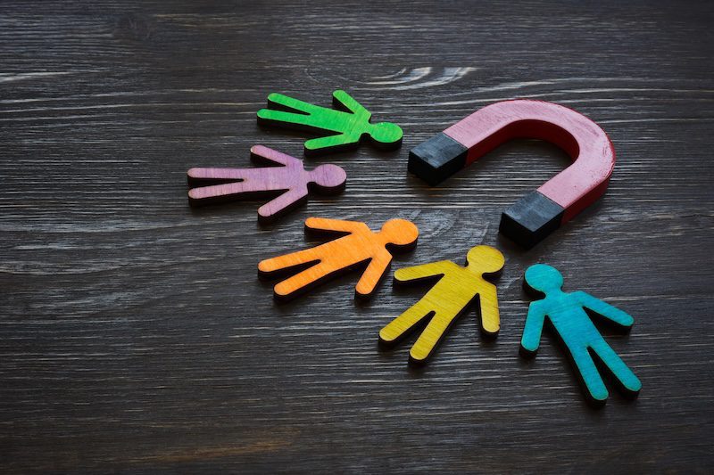 A red horseshoe magnet attracting colorful wooden human figures on a dark wooden surface, symbolizing reputation marketing and the power of attracting people or customers.