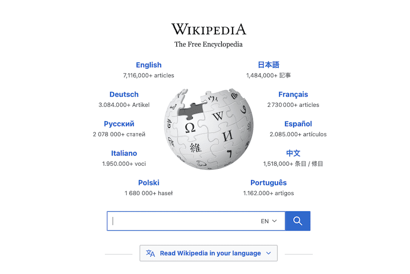 Wikipedia homepage featuring its globe logo and a selection of languages, each with the number of available articles, surrounding the logo. A search bar and "Read Wikipedia in your language" button are below—raising the question: is Wikipedia reliable?.