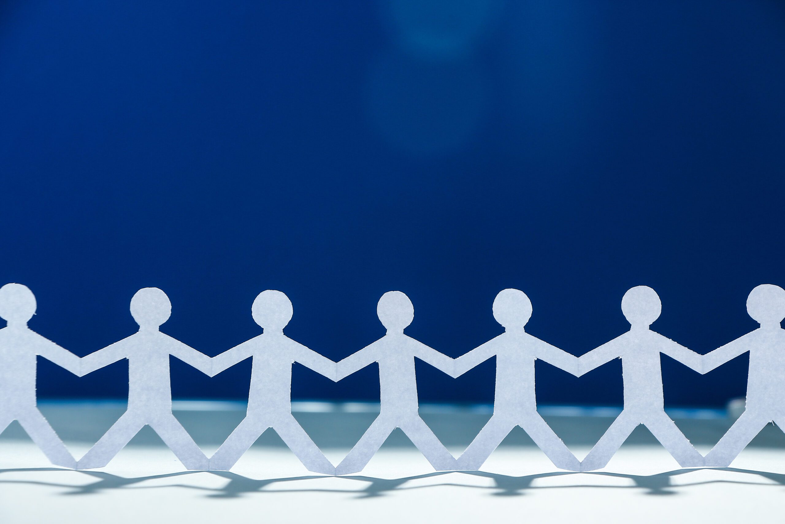 A row of white paper cutout figures holding hands against a blue background, symbolizing unity and teamwork.