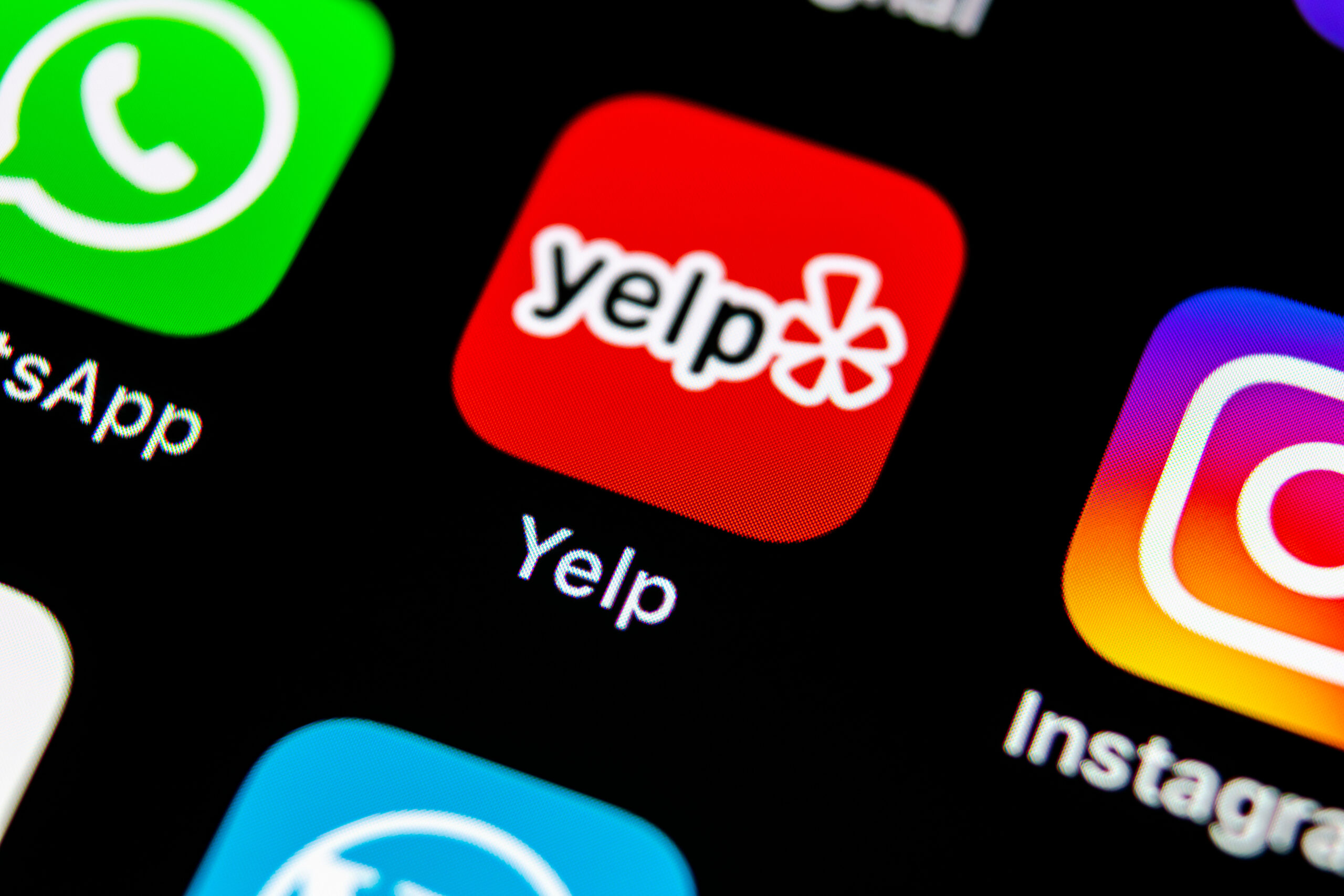 Close-up of a smartphone screen displaying app icons, including WhatsApp (green), Yelp (red with white text and burst), and Instagram (colorful gradient), with the Yelp app centered and in focus.