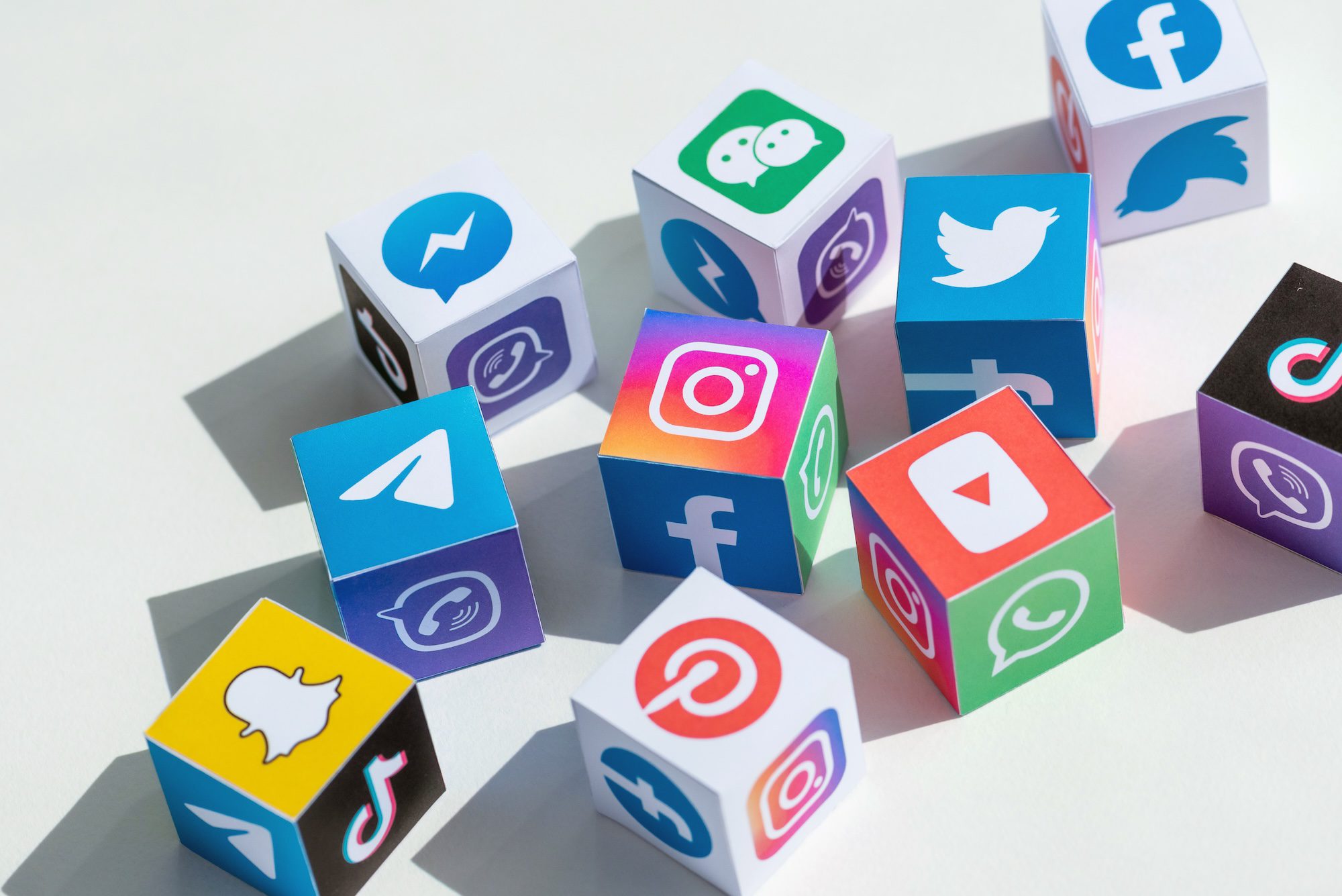 Colorful paper cubes featuring social media icons, including Facebook, TikTok, and more, are scattered on a white surface—perfectly illustrating the role of every social network in marketing today.