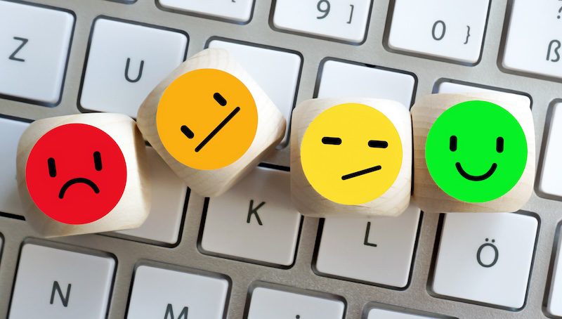 Four wooden cubes with colorful faces showing different emotions rest on a white computer keyboard, symbolizing the range of employee feedback crucial for effective Glassdoor reputation management.