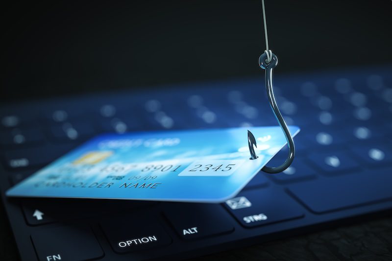 A fishing hook catches a credit card on a computer keyboard, symbolizing online phishing and the importance of executive privacy risk management in combating digital financial scams.