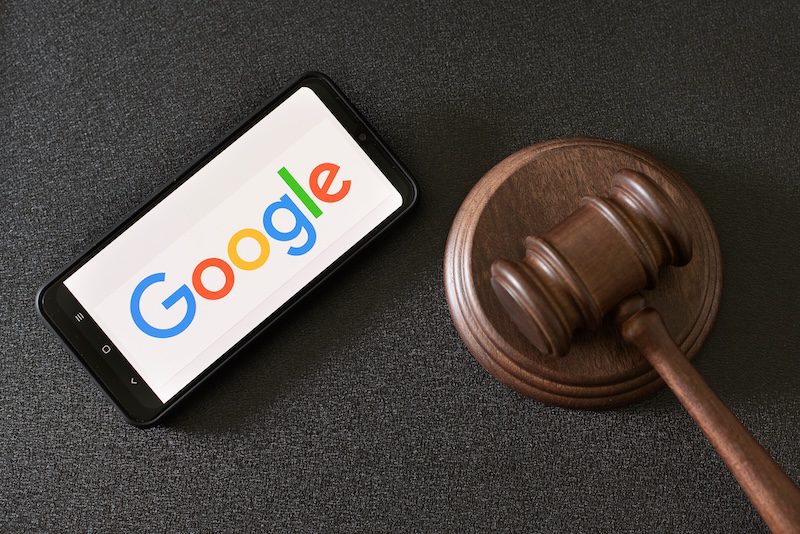 A smartphone displaying the Google logo lies next to a wooden judge’s gavel on a black surface, suggesting a legal issue involving Google and internet defamation removal.